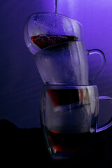 Glass cup with dark hot drink illuminated by purple light, creating moody modern still life.