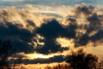 Dramatic sunset sky with a dark cloud resembling a monstrous face. Eerie natural pareidolia amidst golden and dusky hues, sparking imagination