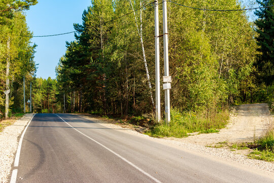Paved road meets a gravel path on a sunny late summer day. Lush green forest lines the quiet route, inviting exploration. Rural junction - Powered by Adobe