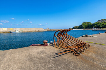 漁船用錨が並べられているひなびた漁港の風景（左側の堤防の文字は「命に着せる救命胴衣」）