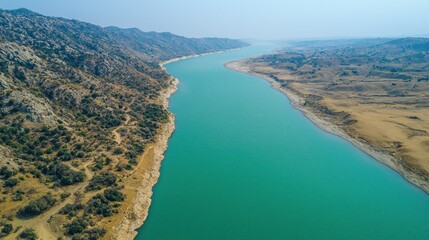 Fototapeta premium Turquoise river winds between rocky hills under bright, hazy sky from above