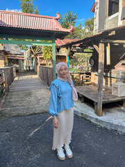 A young woman smiles while standing on a path in a village with wooden houses on a sunny day