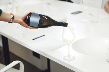 Close-up of sommelier pouring white sparkling wine into wine glass. Training and wine tasting.