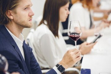 Professional looking sommelier tasting red wine from glass, analysing its taste, color, smell and acidity level. Wine expert studies wine geographic and area on winemaking lecture. 