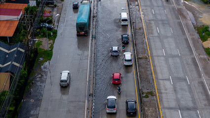 Aerial view of partially flooded road with cars and motorcycles navigating waterlogged areas, representing urban flooding, traffic disruption, and natural disaster impact.
