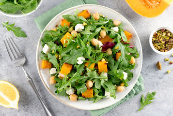 Healthy arugula salad with roasted pumpkin, chickpeas, feta cheese, pistachios on gray background.