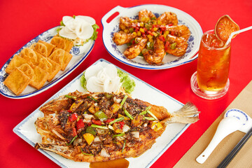 Chinese Seafood Set with Fried Fish, Spicy Prawns, and Tofu Served with Bael Iced Tea on Red Background