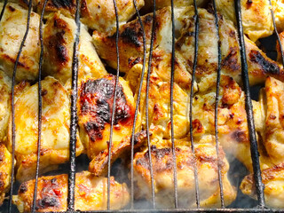 Close-up of chicken pieces grilling on a barbecue grate.