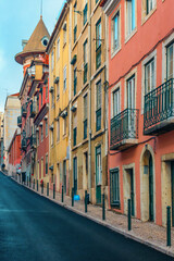 Colorful historic buildings with wrought iron balconies on steep street in Lisbon city, Portugal. City road in old town of Lisboa. Vertical orientation. Travel and tourism in Europe