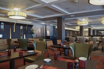 Formal and elegant ocean view a la carte dining room restaurant onboard luxury cruiseship cruise ship liner with set tables in leather and wood Art Deco interior design style ceiling ambient lighting
