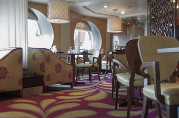 Formal and elegant ocean view a la carte dining room restaurant onboard luxury cruiseship cruise ship liner with set tables in leather and wood Art Deco interior design style ceiling ambient lighting