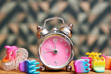 A retro-style silver alarm clock with a pink face is surrounded by colorful hair ties and toe separators