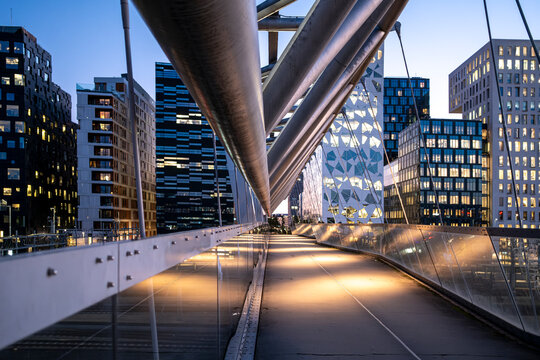 Modern architecture of the Akrobaten bridge in Oslo and Barcode skyline captured in panoramic perspective at evening with steel geometry, soft light and urban reflections