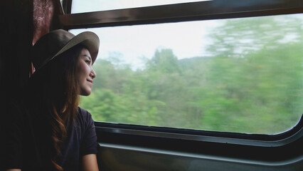 A female train passenger looking at the trees and forest views outside window © Farknot Architect
