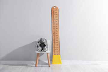 Height measuring chart on light grey wall and toy bunny indoors