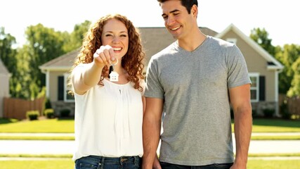 Happy couple holding house key outside their new home in sunlight  