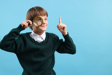 Little boy with magnifying glass on light blue background. Space for text