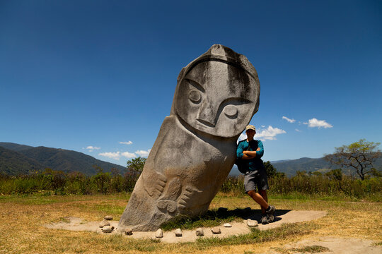 Western male tourist, poses with the Palindo megalith, located in the Bada Valley, Central Sulawesi, Indonesia