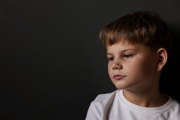 Upset little boy on black background, space for text