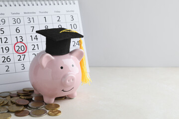 Education savings plan. Piggy bank with graduation cap, coins and calendar on light table, space...