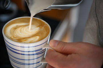 A person pouring steamed milk into a coffee cup creating intricate latte art at home.