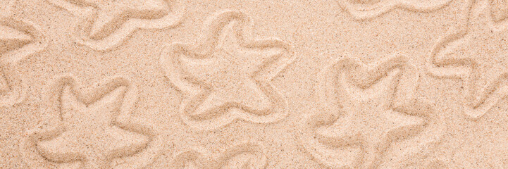 Starfish shapes pattern on dry light brown sea sand background. Closeup. Wide banner. Top down view.