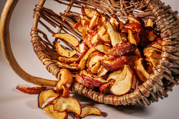 An overturned wicker basket with scattered slices of dried apples, revealing their crunchy texture and naturally red skin in the warm lighting.