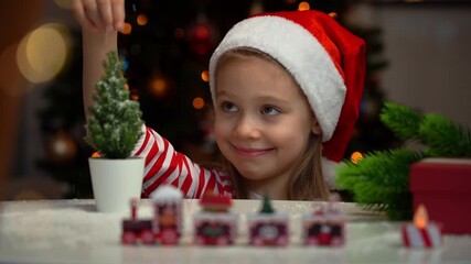 Portrait of happy little girl sprinkles toy fir with snow on background of Christmas tree. Christmas gift present box. Christmas New Years