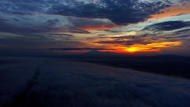 Aerial view of a stunning sunrise over a sea of clouds with a lawu mountain silhouette in the distance, creating a beautiful contrast of colors, Klaten Regency, Indonesia.