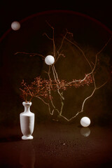 Still life with a branch of a plant in a white vase and white balls on a dark background