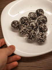 A hand holds a plate with healthy chocolate coconut balls. Vegan, homemade dessert.