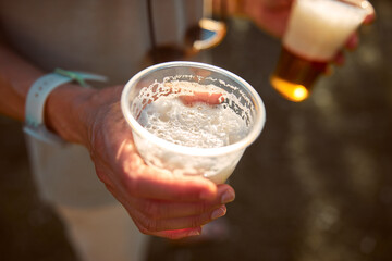 Person holding beer cup outdoors on a sunny day.