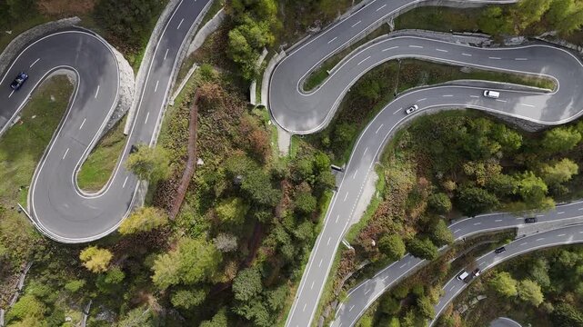Aerial view of a winding road with cars cutting through the mountainous terrain with lush green trees, Bregaglia, Grisons, Switzerland.