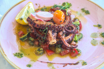 Delicious octopus dish served with lemon, vegetables and sauce in a restaurant