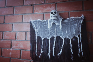 A close-up of a Halloween grim reaper with a skull face and ragged gauze cape attached to a red...