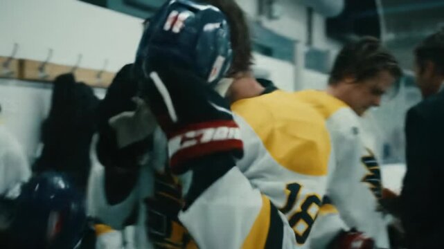 Determined male ice hockey coach in dark suit delivers aggressive speech to young male players (18-22) in white/yellow jerseys preparing in gritty locker room under harsh lights, intense pre-game