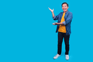 Full Body of Smiling Asian Male Presenting Aside for Ads on Blue Studio Background