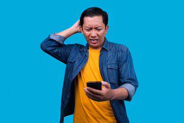 Confused Young Guy Looking At Smartphone Over Yellow Studio Wall