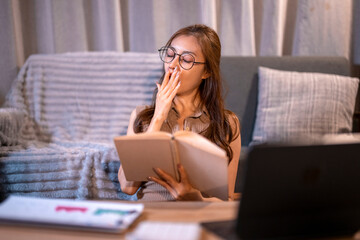 Tired woman yawning while studying at night
