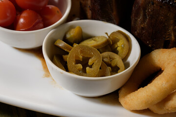 plates with marinated tomatoes, pickled green hot peppers and teriyaki sauce for a meat dish
