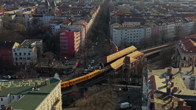 Aerial view of a yellow subway crossing schlesisches tor station in the city, surrounded by buildings, cars, and leafless trees, Berlin, Berlin, Germany.