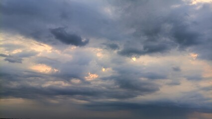 Dramatic cloudy sky with soft golden light breaking through thick gray clouds before a rainstorm, perfect for themes of climate, tranquility, or changing weather