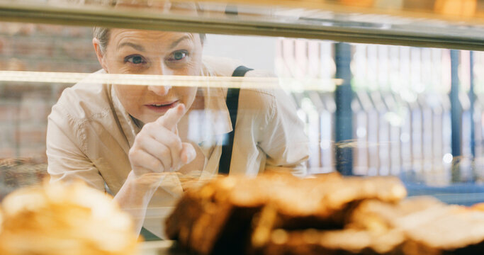 Bakery, window and woman with choice with cake, donuts and pastry options in restaurant and cafeteria. Breakfast, mature person and snack in coffee shop for food, dessert products and sweets treat