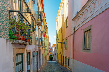 Colorful narrow street with traditional azulejo tiled buildings and balconies in Lisbon city, Portugal. Medieval alley in old town of Lisboa. Travel and tourism in Europe. Portuguese architecture