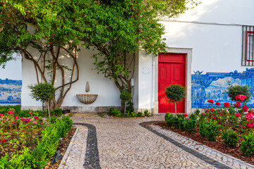 Traditional Portuguese garden with mosaic stone path, red door, blue azulejo tiles and blooming roses in Lisbon city, Portugal. Medieval alley in old town of Lisboa. Travel and tourism in Europe