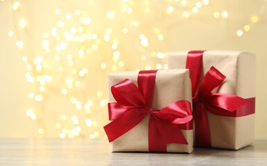 Wrapped gifts with red ribbons on table with bright bokeh behind