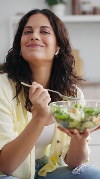 Video of beautiful woman eating healthy salad while looking at camera in the kitchen at home