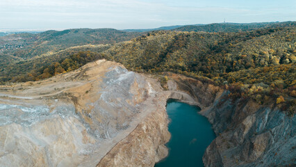 Aerial view of a flooded quarry surrounded by colorful autumn forest in Fruska Gora, Serbia. Calm turquoise water contrasts with rocky cliffs and seasonal foliage