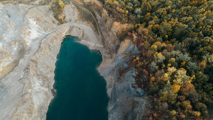 Horizontal top down aerial view of colorful autumn forest and steep rocky slope above turquoise lake in Fruska Gora, Serbia. Contrast between nature and geology