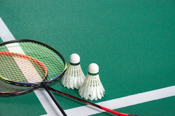 A pair of badminton rackets and two shuttlecocks are arranged on the green court near the white boundary lines, showing the gear ready for a match or practice session.